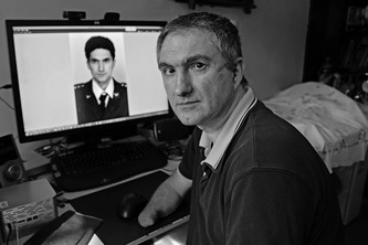 Branislav Kapetanović schaut ernst in die Kamera, hinter ihm ein Computerbildschirm mit einem Bild von ihm als junger Mann.