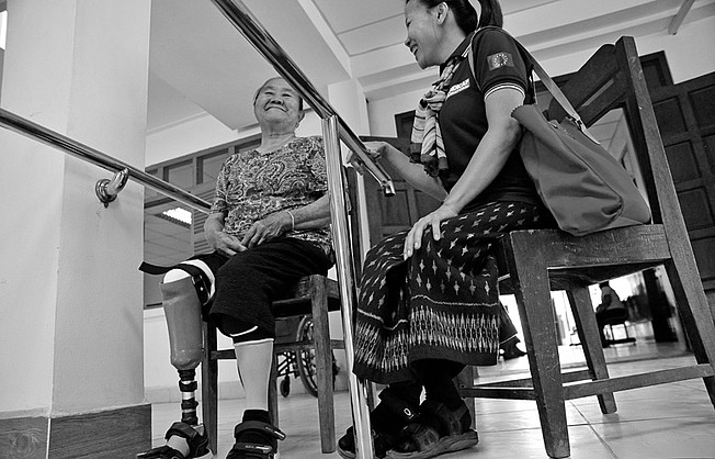 Eine Frau mit Beinprothese sitzt zwischen zwei Barren. Neben ihr eine Mitarbeiterin von HI.